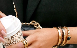 Fashionable layered gold rings and bracelets styled with a black jacket and coffee