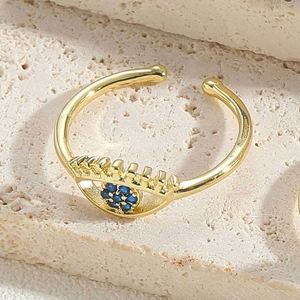 Detailed close-up of a gold Evil Eye ring with blue and clear zircon on a stone surface