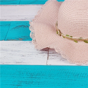 Detail of pink straw sun hat with wavy edges and decorative green leaves on wood