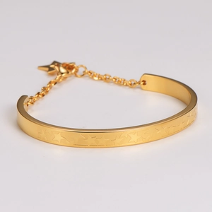 Detalle de brazalete dorado con estrellas grabadas, cierre de cadena y colgante de estrella