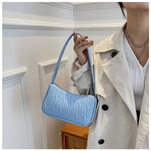 Close-up of blue quilted PU leather shoulder bag with wavy texture held by a model