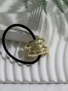 Macro detail of a hammered gold metal ring on a black elastic ponytail holder