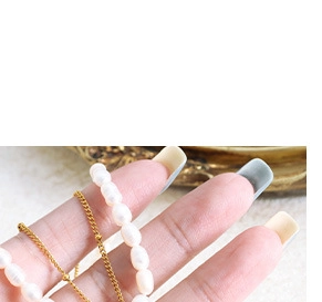 Close-up of elegant gold chain and white pearl necklace held on fingertips