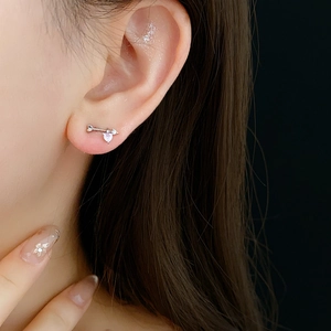 Close-up of a silver cupid arrow stud earring with zircons on a model's ear