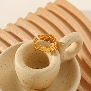 Detail of golden leaf-shaped stainless steel ring displayed on a ceramic cup handle