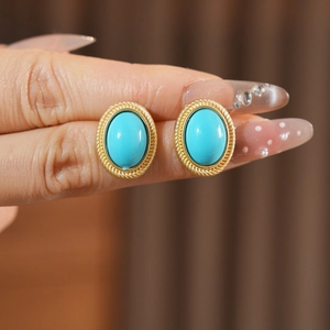 Close-up of vintage oval turquoise earrings with gold twisted rope border held by hand