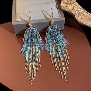 Close-up of emerald and diamond leaf tassel earrings on a brown leather surface