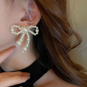 Elegant bow-shaped faux pearl drop earrings worn by a model in a close-up detail shot