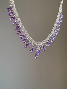 Close-up of silver necklace featuring purple teardrop pendant and shimmering diamonds