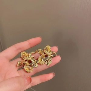 Macro detail of irregular golden flower stud earrings with a textured metallic finish