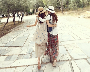 Women in summer long dresses and straw sun hats with bows walking in a scenic park