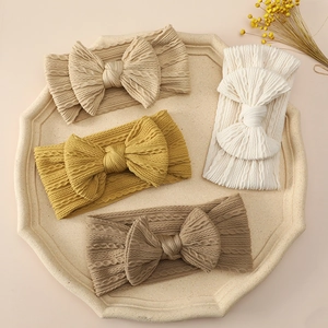 Set of four knitted baby bow headbands in neutral colors on an octagonal plate