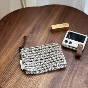Detail of hand-woven striped pouch showing zipper and rope handle on wooden desk