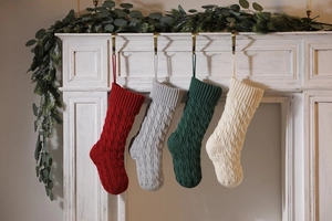 Close-up of four knitted Christmas stockings with cable patterns on a white fireplace