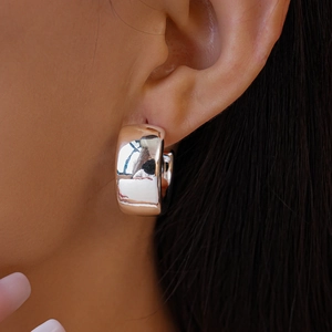 Close-up of chunky silver C-shaped hoop earrings with a polished mirror finish on model