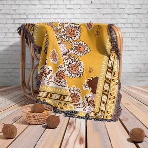 Detail of bohemian knit blanket with yellow floral patterns and fringe on a rattan chair