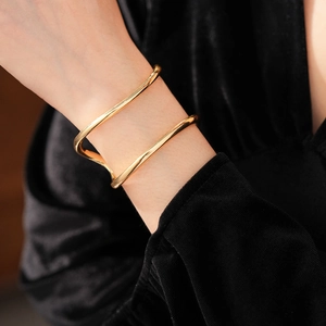 Détail d'un bracelet ouvert doré à double couche irrégulière porté sur un poignet