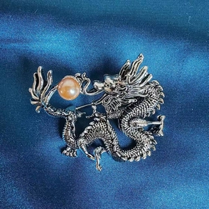 Detailansicht der silbernen Drachenbrosche mit Bernsteinperle auf blauem Satin
