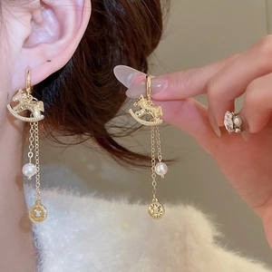Détail de boucles d'oreilles cheval de Troie avec glands dorés, perles et pièces de monnaie