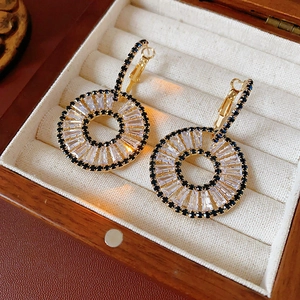 Detail of gold-tone geometric hoop earrings with clear zircons and dark gemstones