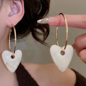 Golden hoop earrings with marble heart pendant worn by a model in warm light
