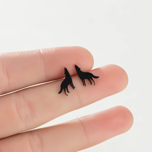 Macro detail of matte black wolf-shaped stud earrings held by hand to show compact size