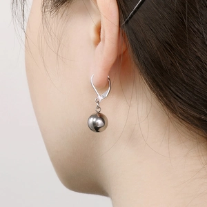 Minimalist stainless steel oval hoop earrings with silver ball pendant on female model