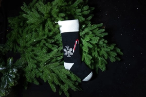 Detail of black knitted Christmas stocking with white snowflake and candy cane patterns