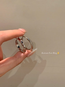 Detailed view of minimalist silver hoop earrings held by hand against a beige background