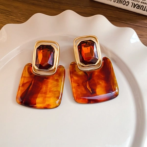 Detailed view of amber resin square earrings with gold frames on a white ceramic plate