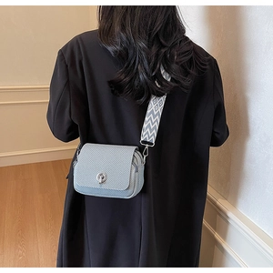 Detailed view of a mini textured crossbody bag with wide patterned strap and metal twist lock.