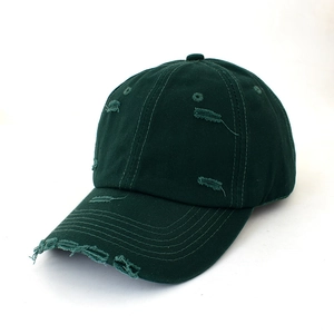 Detail of distressed hole design on dark green vintage washed canvas baseball cap