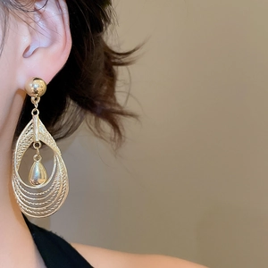 Close-up of elegant layered gold teardrop earrings worn by a model in warm light