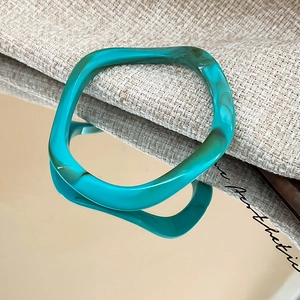 Macro detail of teal marble resin bangle with irregular wavy texture on mirror