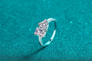 Macro shot of silver ring featuring heart and emerald cut moissanite on blue glitter