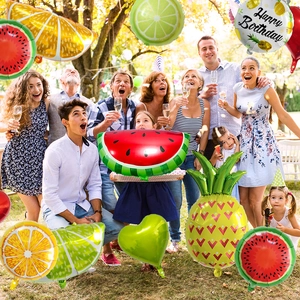 Outdoor birthday party scene featuring giant fruit-shaped foil balloons in a garden