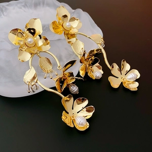 Macro shot of gold floral earrings with pearls and delicate metallic petals on dark background