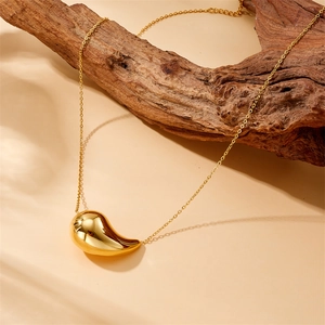 Détail macro du collier à pendentif goutte dorée sur bois flotté et lumière douce