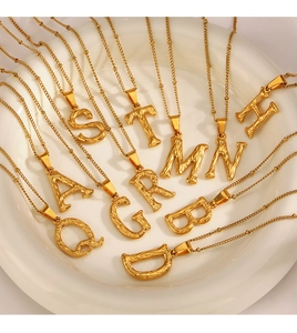Detailed display of gold alphabet pendants with hammered texture in a white ceramic tray