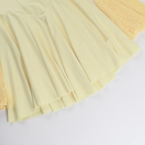 Close-up of yellow dress showing lace cuffs and pleated hem details on white background