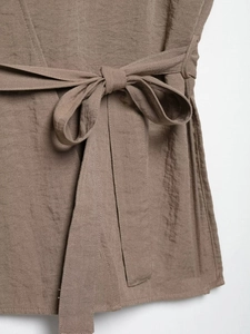Dettaglio dei pantaloni in lino marrone caffè con fiocco in vita e texture naturale
