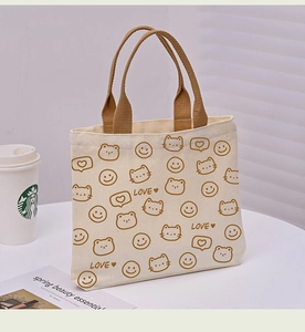 Detailed close-up of beige canvas tote bag with cute cat print and brown handles