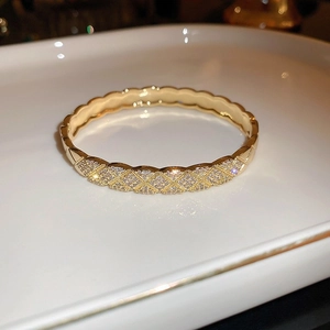 Detailed view of golden lattice bangle with micro-paved cubic zirconia on white tray