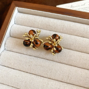 Detailed shot of golden flower earrings with tiger eye beads on beige velvet cushion
