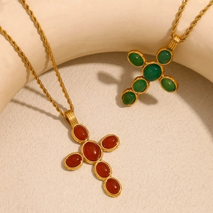 Close-up of gold cross pendants with green and reddish-brown gemstones on rope chains