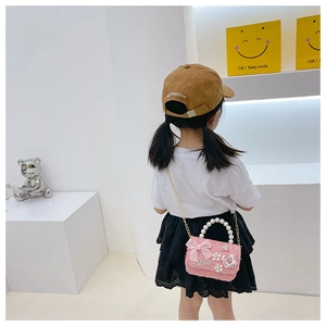 Détail du sac fille en tweed rose avec poignée en perles et chaîne dorée sur fond blanc