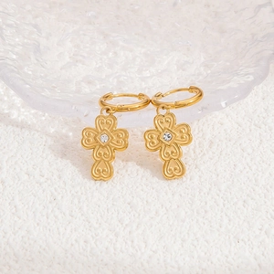 Detail of gold cross earrings with zircon stones on a white marble and glass background