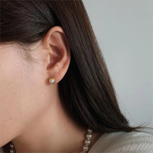 Detail shot of a minimalist gold-framed pearl earring worn on the earlobe