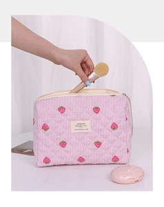 Detailed shot of hand putting brush into strawberry quilted cosmetic bag with pink stripes