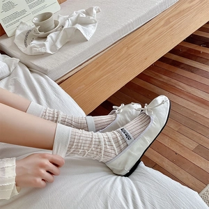 Close-up of ballet-style white Mary Jane shoes with ribbons and striped mid-calf socks